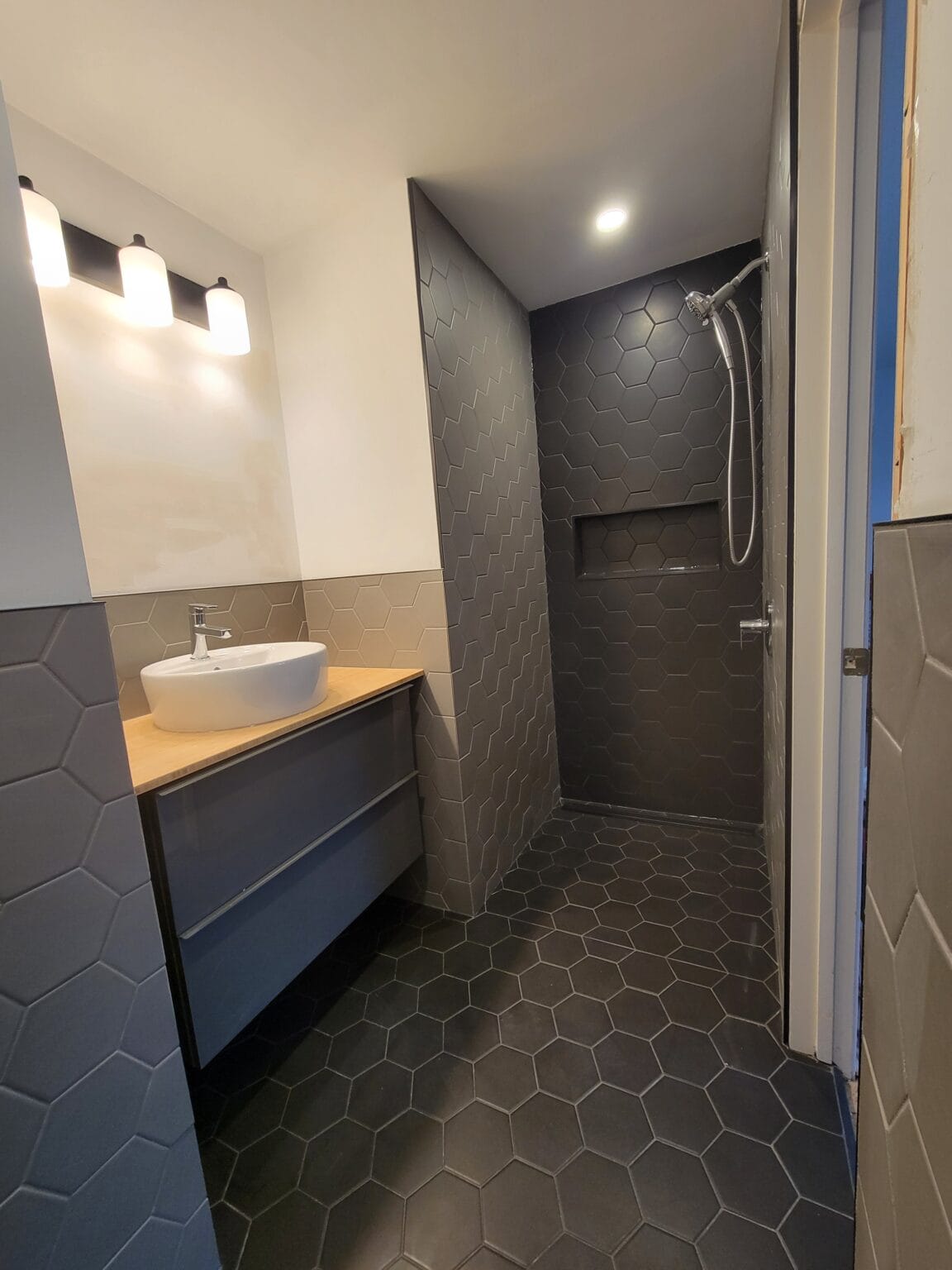 A walk-in shower with dark hexagon tile and a wood vanity